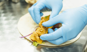 Knuspriges Hähnchenstück wird mit Salat, Käse und Zwiebeln in einen Wrap gelegt
